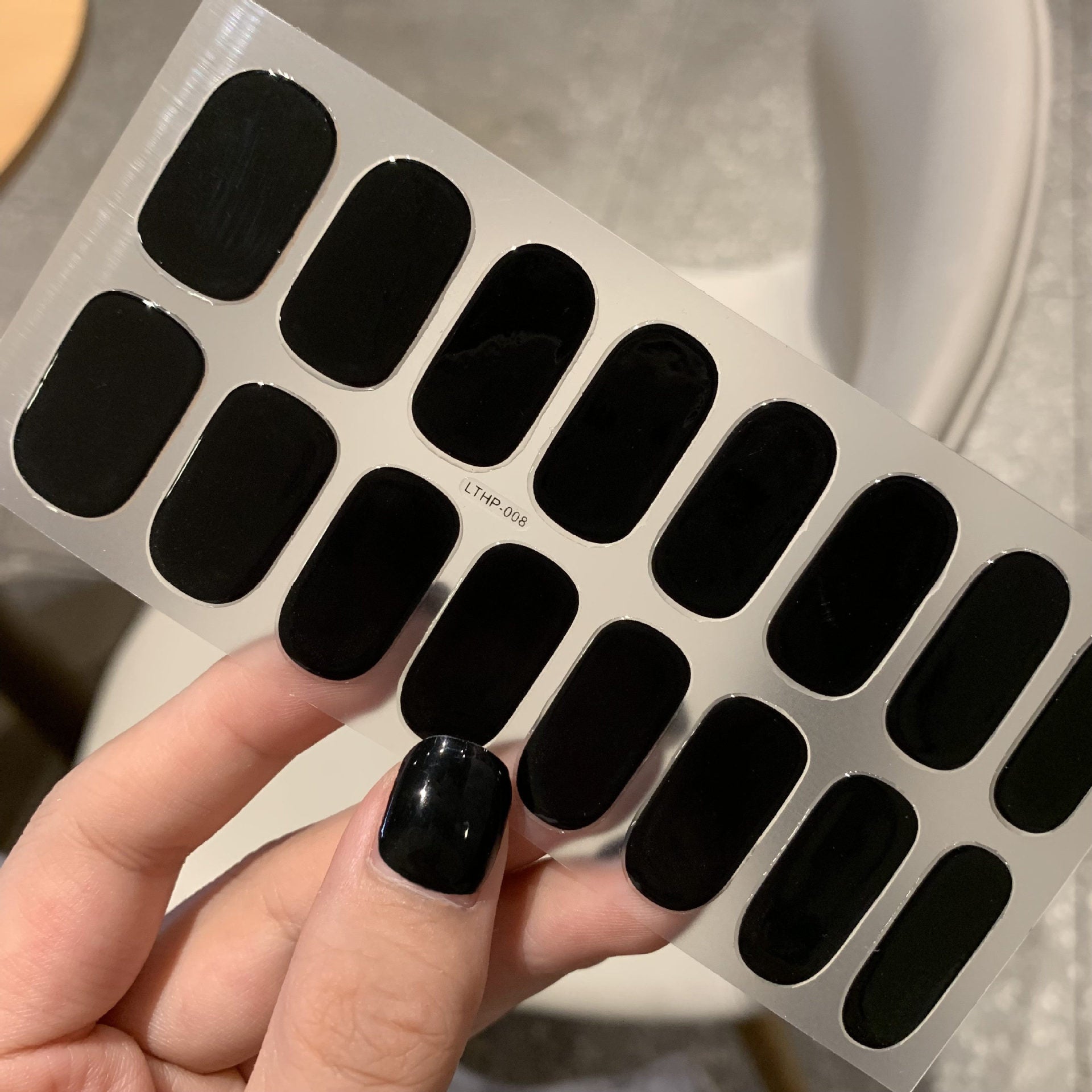 THE SOLID 10-DAY nail stickers in black held by a hand.